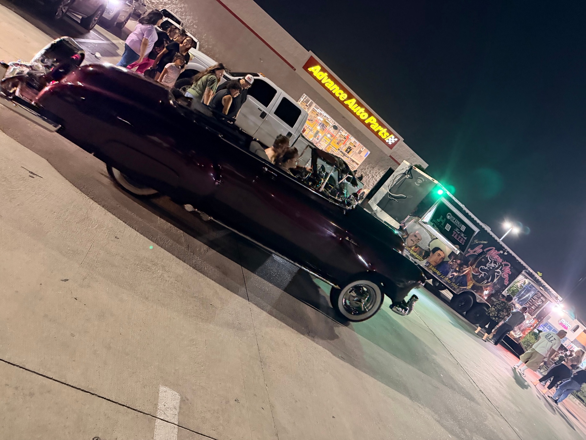 Vintage convertible lowrider rolling by families at the meet
