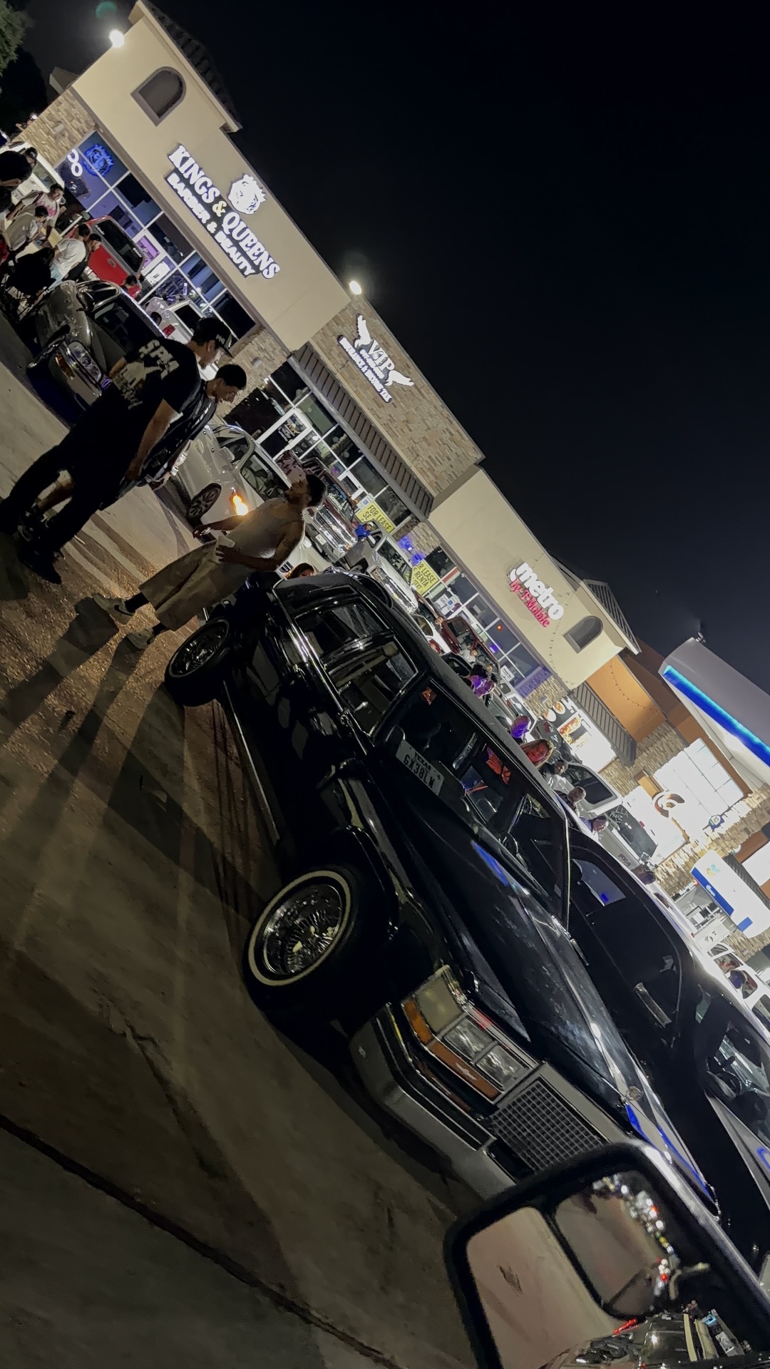 Black Cadillac lowrider parked curbside with the night crowd