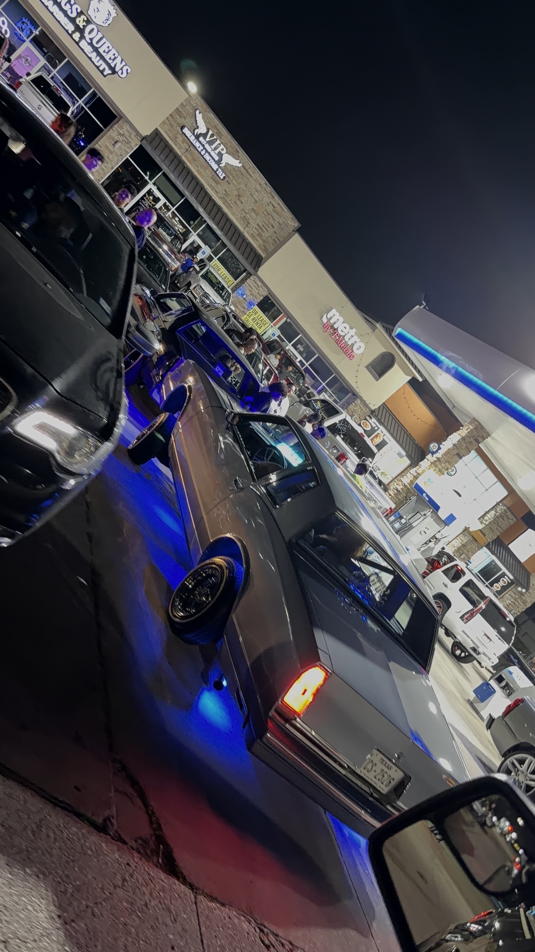 Silver Cadillac with blue underglow lighting up the night meet